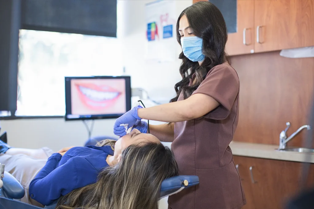 Dental assistant in brown scrubs scanning a reclining patient's teeth