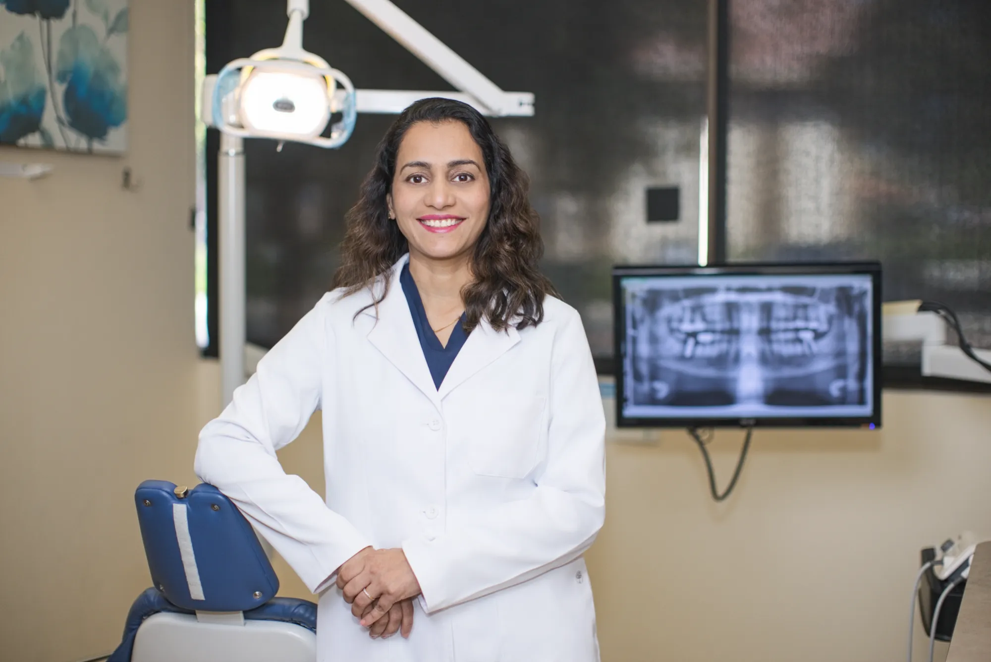 Dr. Trivedi in a white lab coat standing beside the dental chair