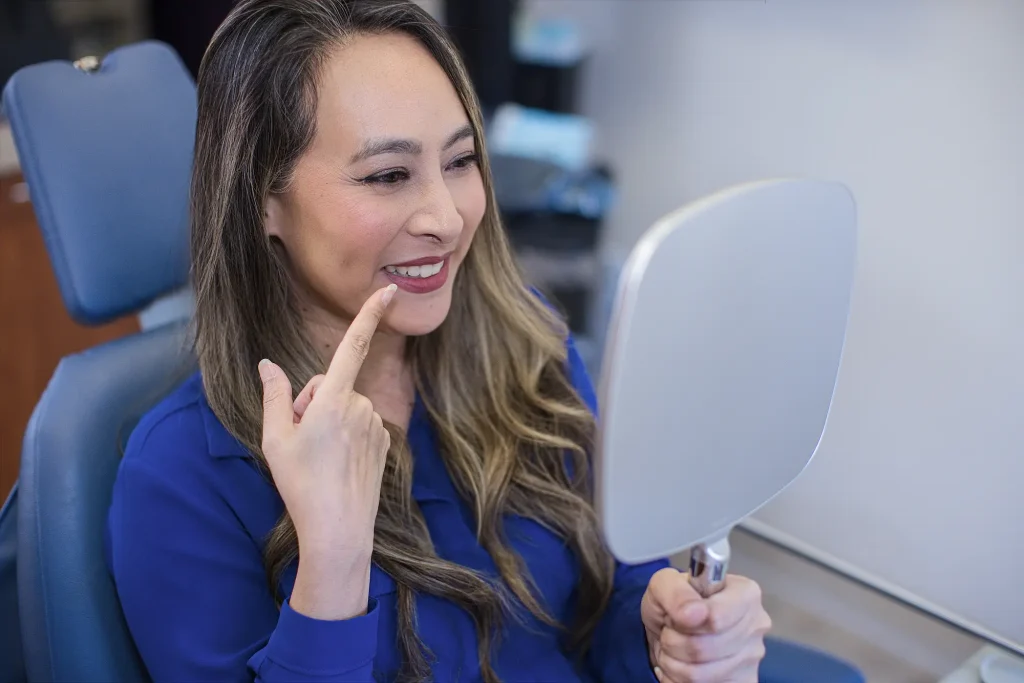 Patient pointing to her smile while holding a hand mirror