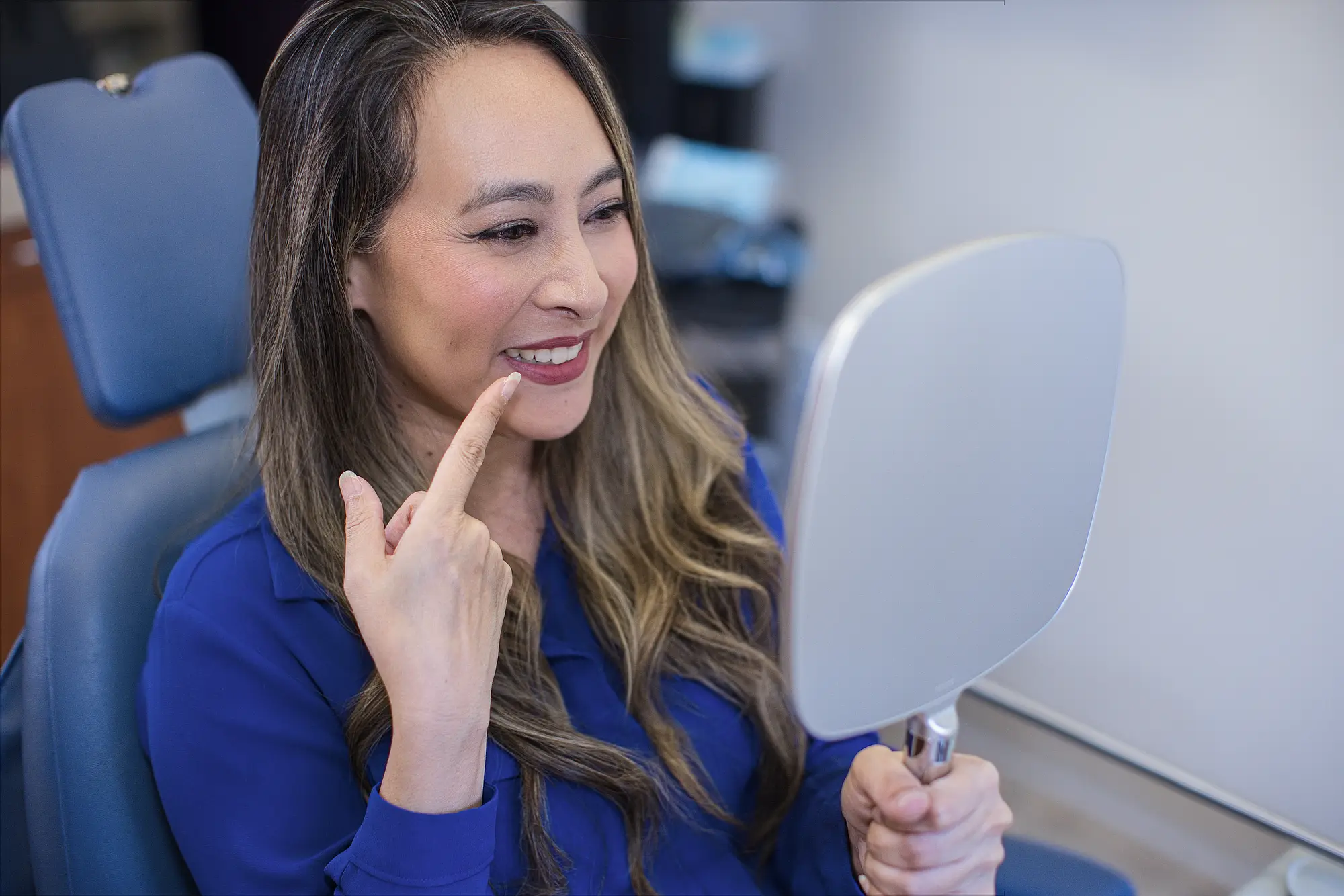 Patient pointing to her smile while holding a hand mirror