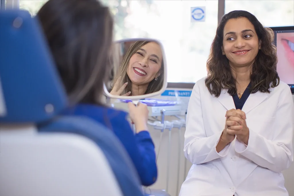 Patient seeing her smile in a hand mirror beside Dr. Trivedi