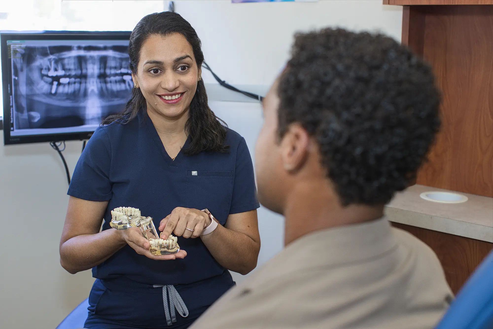 Dr. Trivedi explaining a dental model to a patient beside an X-ray screen