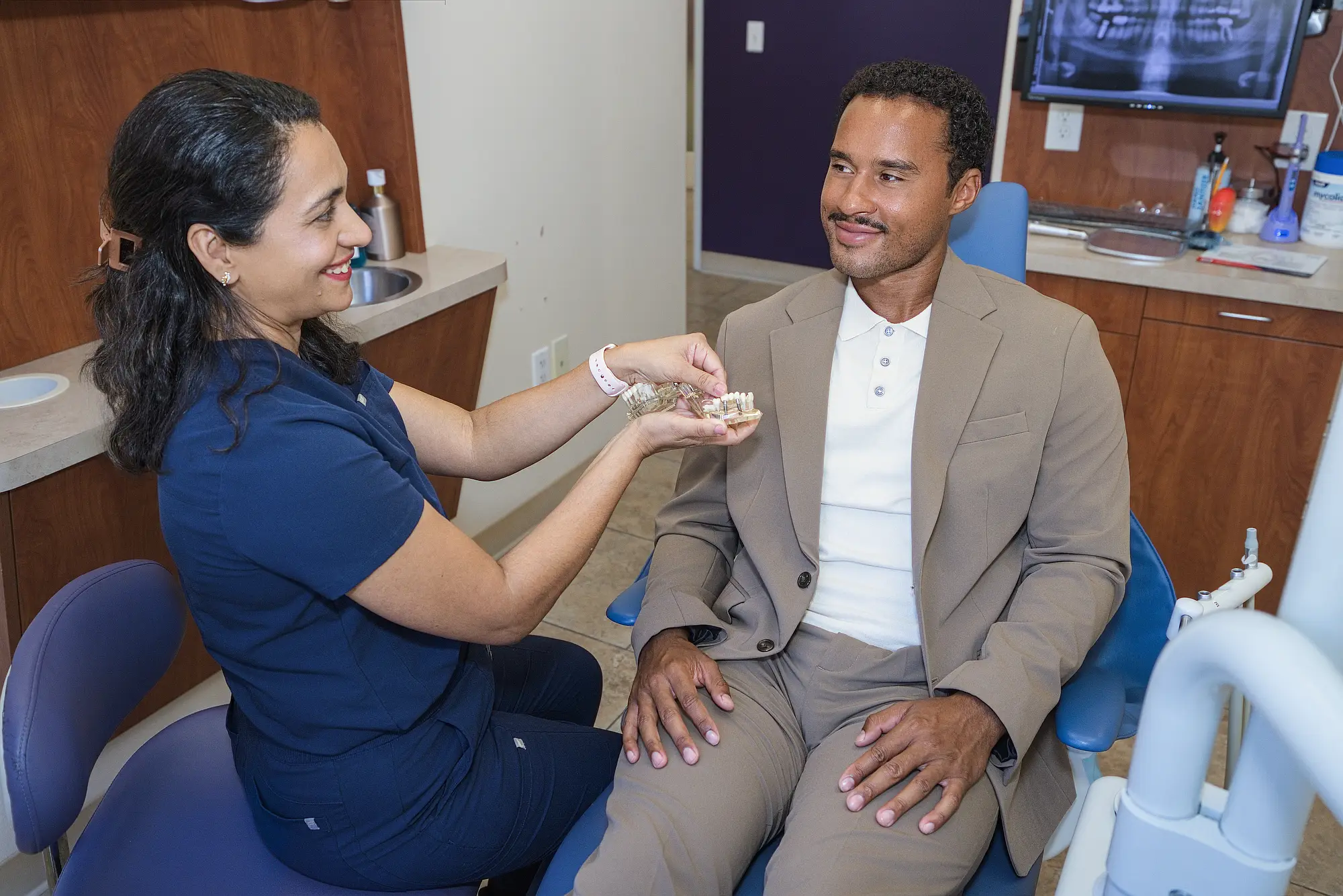 Dr. Trivedi showing a patient a dental implant model in the treatment room