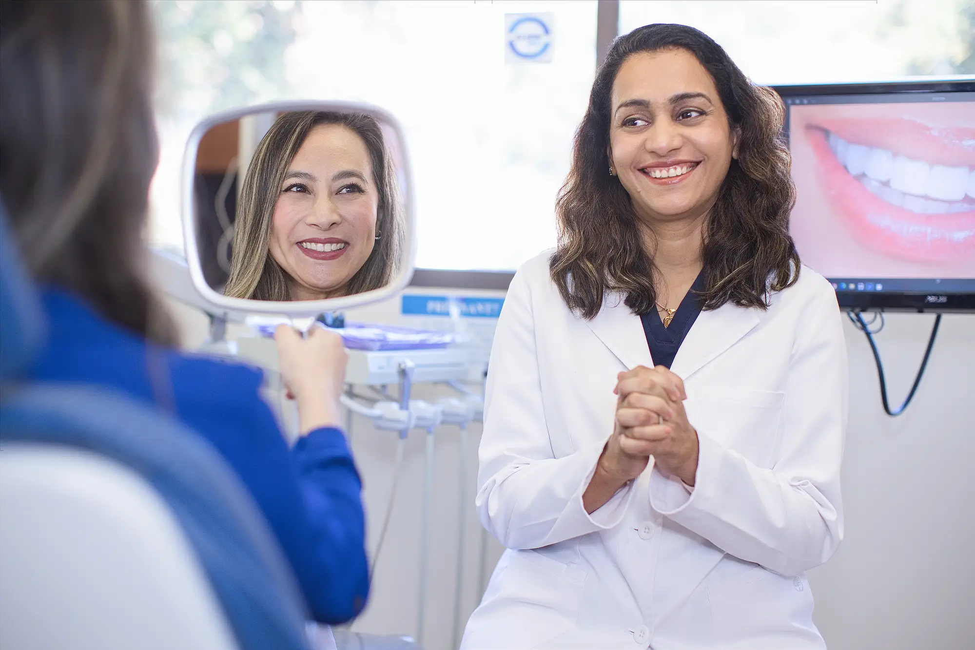 Dr. Trivedi smiling as a patient views her new smile in a hand mirror