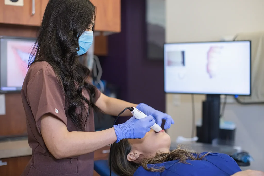 Dental assistant scanning a patient's teeth, with the scan shown on a monitor