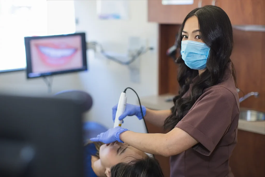 Dental assistant in a mask using an intraoral scanner, a smile shown on screen