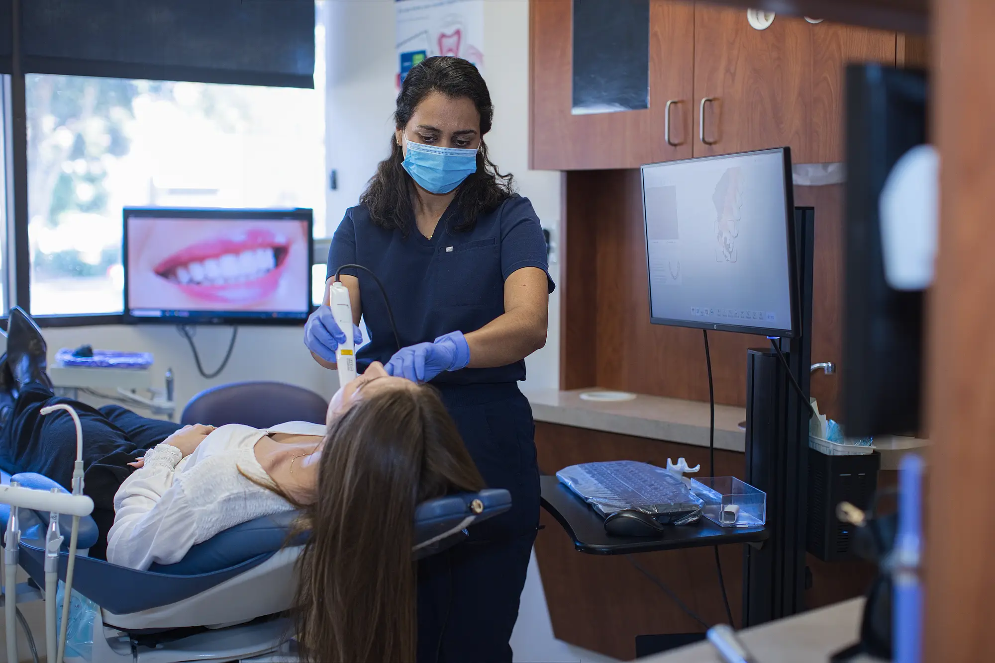 Dental assistant scanning a reclining patient's teeth with an intraoral scanner