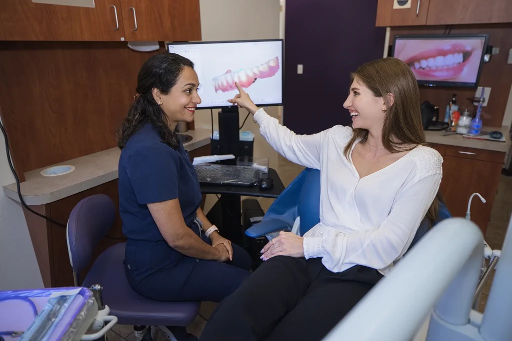 Dr. Trivedi seated beside a patient who points to a smile on the treatment room monitor