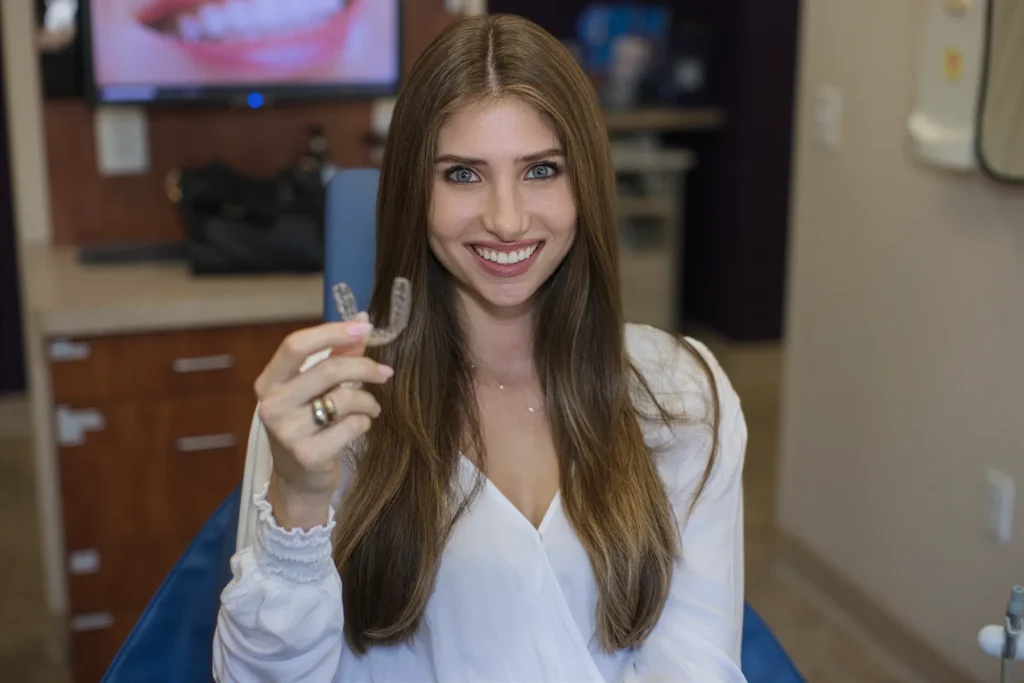 Smiling young woman holding a clear aligner