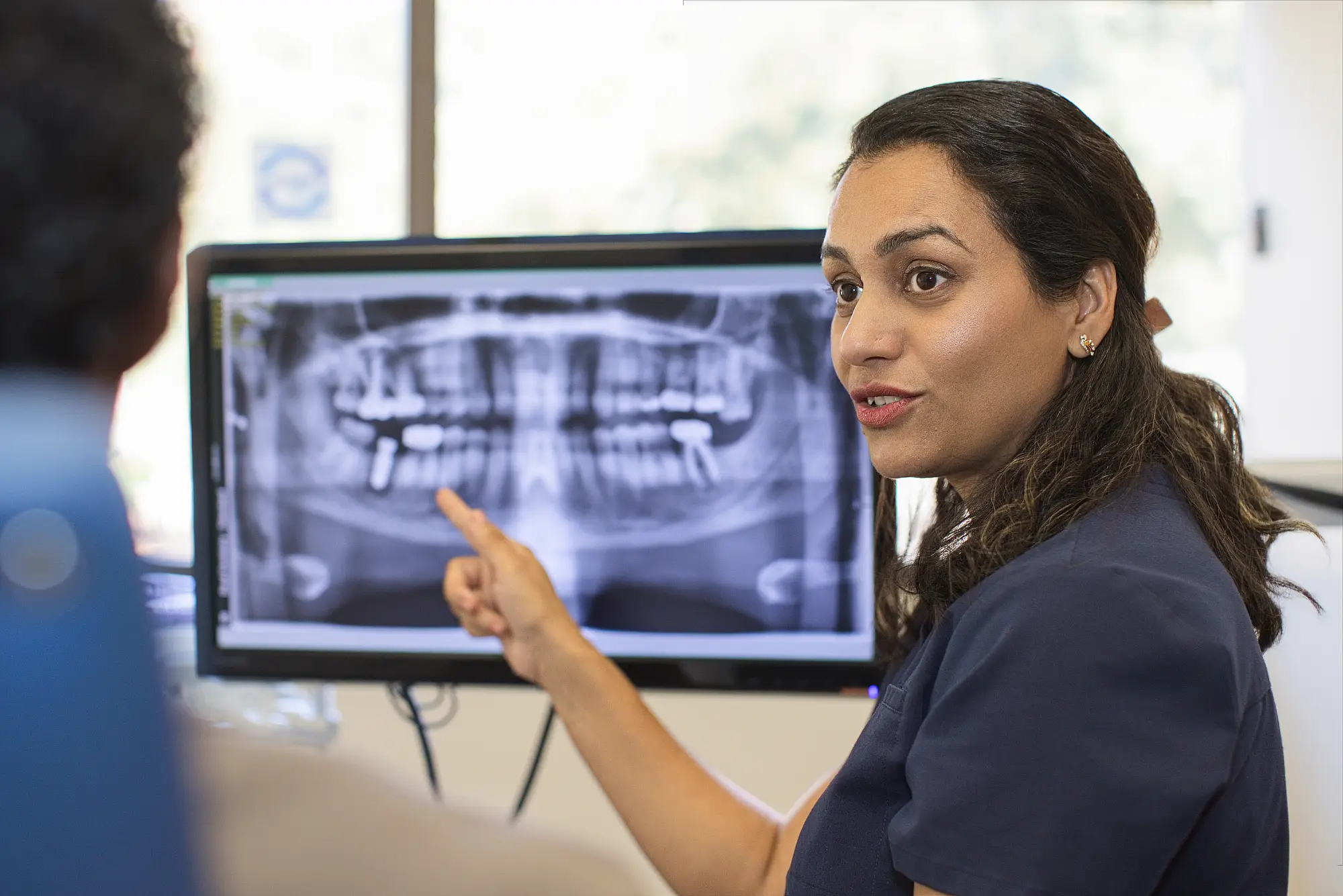 Dr. Trivedi pointing to a panoramic X-ray on a monitor as she talks with a patient